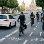 Radfahrende auf einem breiten Radweg in einer deutschen Innenstadt, ein Auto überholt mit Abstand