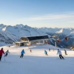 Saisonstart in den Alpen: Erste Skifahrer auf einer frisch präparierten Gletscherpiste vor schneebedeckten Berggipfeln